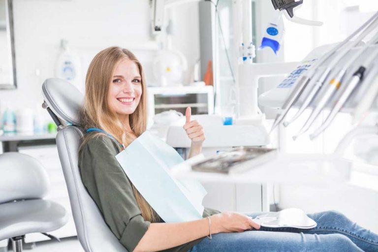A woman in a dentists chair giving a thumbs up.